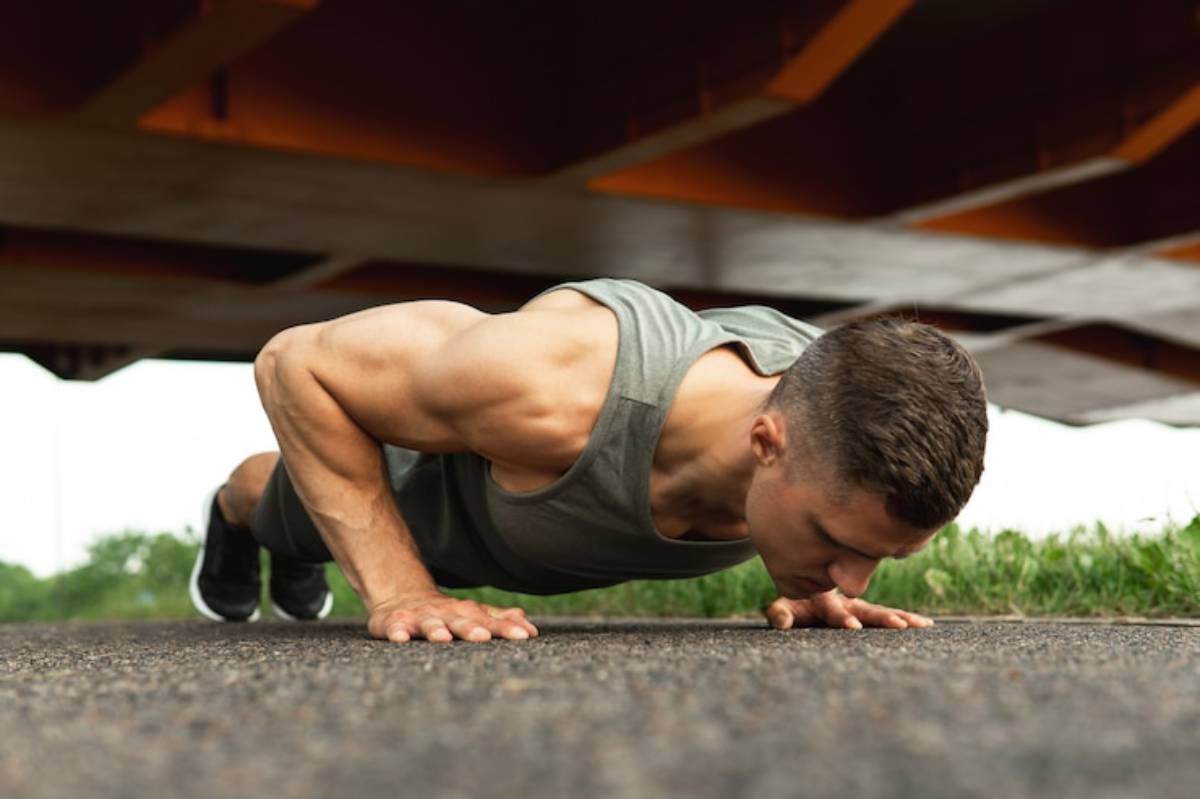 A fitness enthusiast performs push-ups on a textured surface beneath a large structure, showcasing strength and determination.