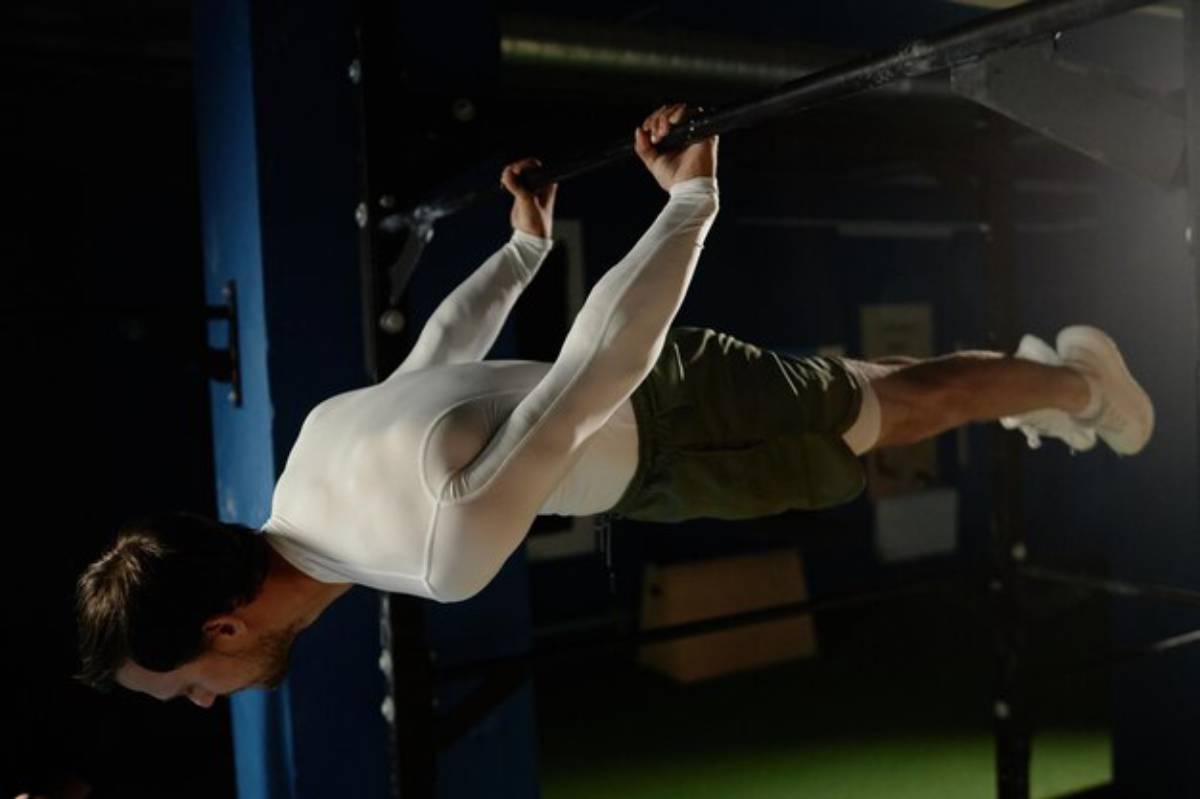 A person performs a dynamic exercise on a pull-up bar, showcasing strength and form against a dark gym background.