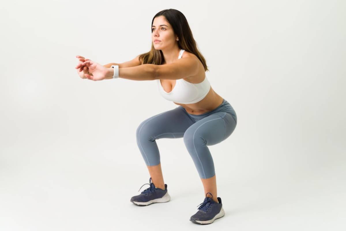 A person is performing a squat in athletic attire, demonstrating proper form with feet shoulder-width apart and arms extended forward.