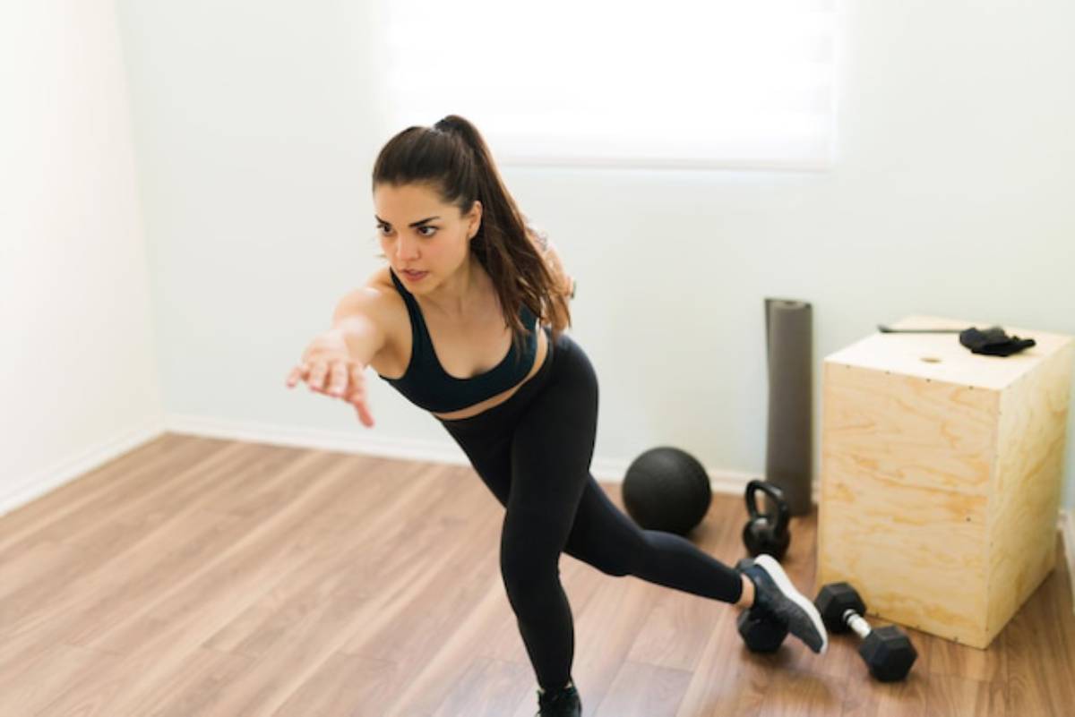 A person in athletic attire performs a dynamic workout move in a bright, minimal home gym, surrounded by fitness equipment.