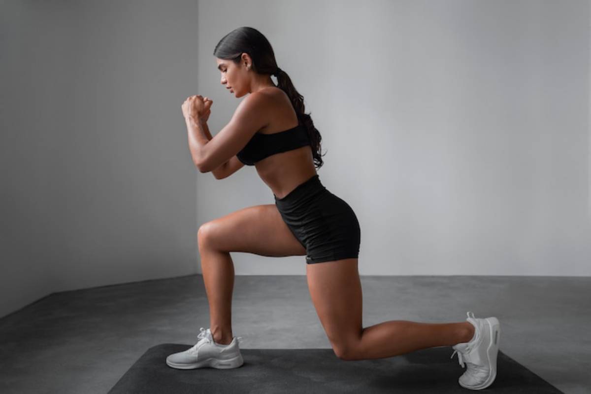 A fit individual in activewear performs a lunge on a mat, showcasing strong leg muscles and a focused posture in a minimalistic setting.