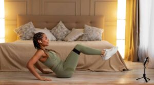 A person in green athletic attire performs a workout at home, with a neatly made bed and soft lighting in the background.