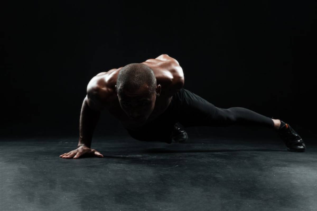 A muscular athlete performing a push-up on a dark stage, showcasing strength and determination. Dramatic lighting highlights their physique.