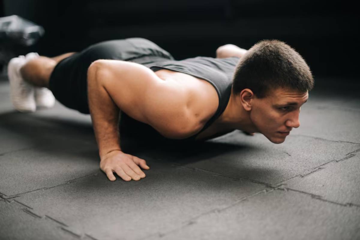 A muscular individual performs a push-up on a black rubber mat in a dimly lit gym, showcasing strength and focus.