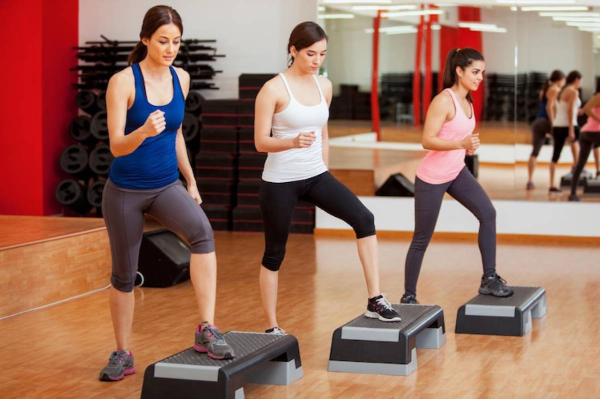 Three women are exercising on step platforms in a bright fitness studio, focusing on their workout routines.