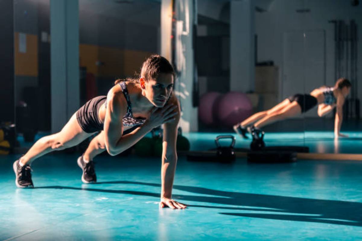 A fit individual performs mountain climbers on a gym floor, surrounded by exercise equipment and colorful workout balls.