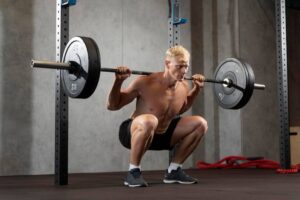 A muscular individual performing a barbell squat in a fitness studio, with weights on the bar and a focused posture.