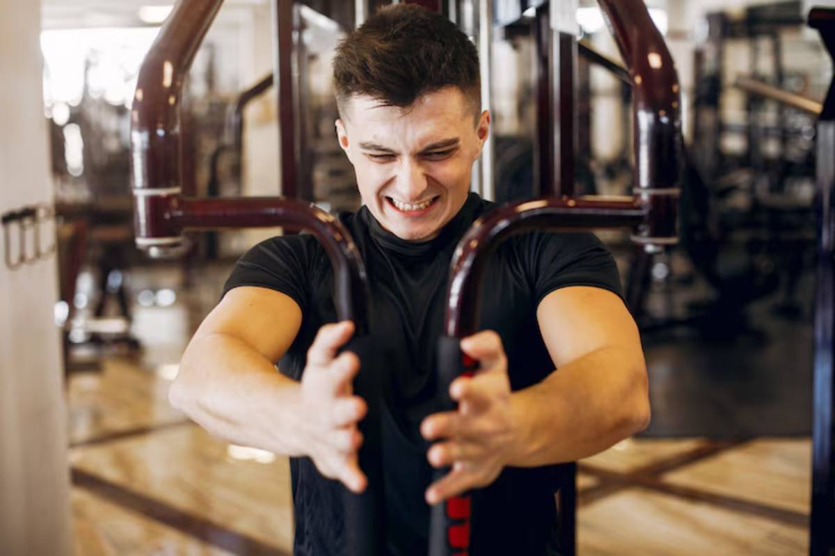 A young man in a black shirt engages in strength training at a gym using a machine, focused on his workout.