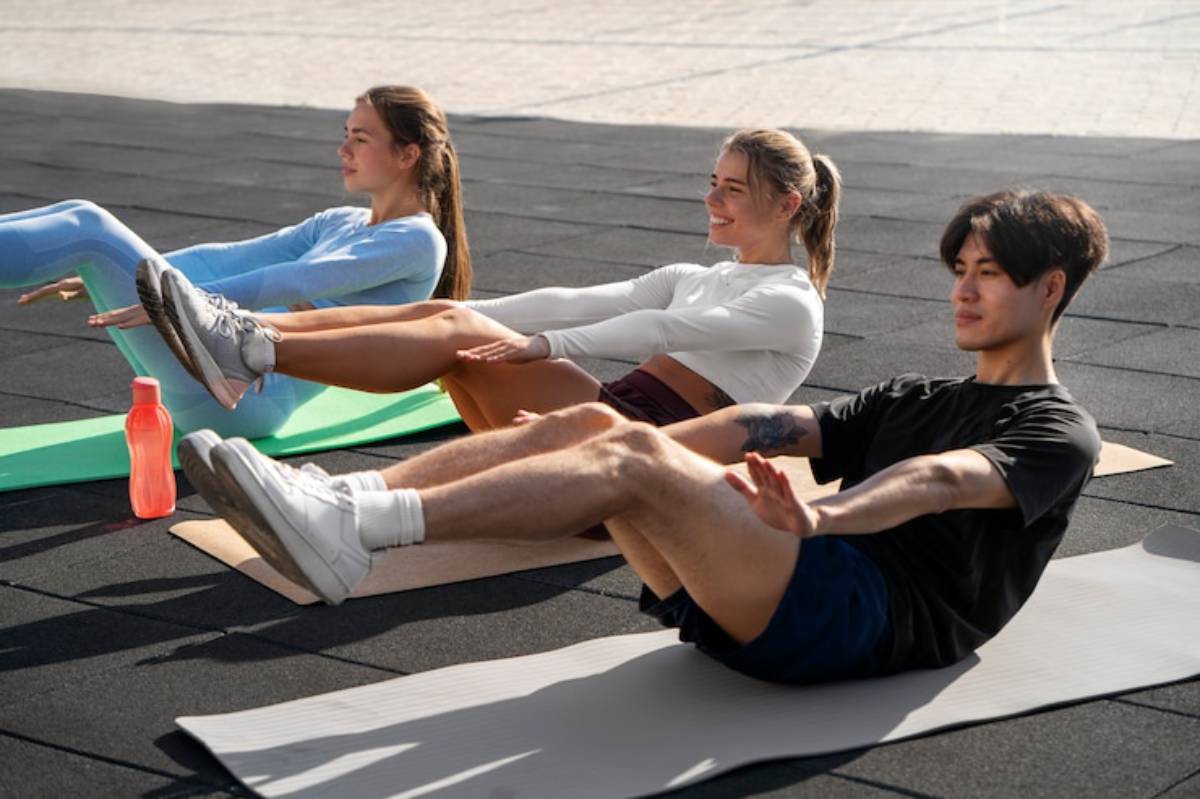Three individuals practice core exercises on mats at an outdoor fitness session, with water bottles nearby.