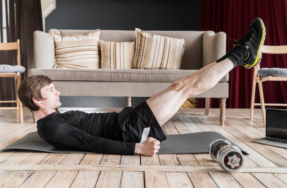 A person in a black workout outfit performs leg lifts on a yoga mat in a stylish indoor space with a couch and weights nearby.