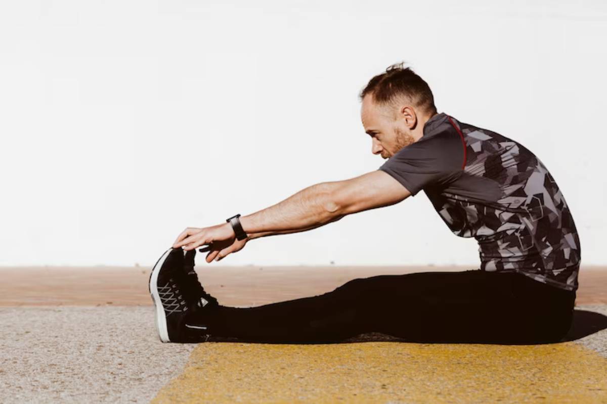 A person in athletic wear stretches forward to touch their toes on a sunny outdoor surface, promoting flexibility and fitness.