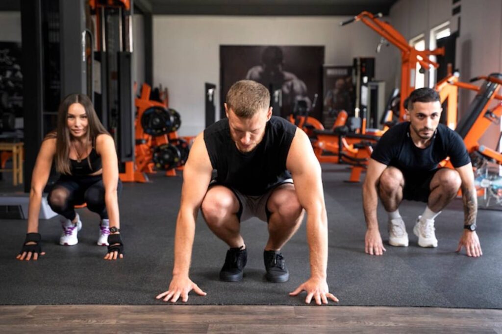 Three individuals are positioned in a fitness studio, preparing to start an exercise, showcasing their athletic attire and focus.