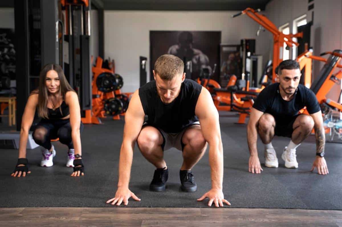 Three individuals are positioned in a fitness studio, preparing to start an exercise, showcasing their athletic attire and focus.