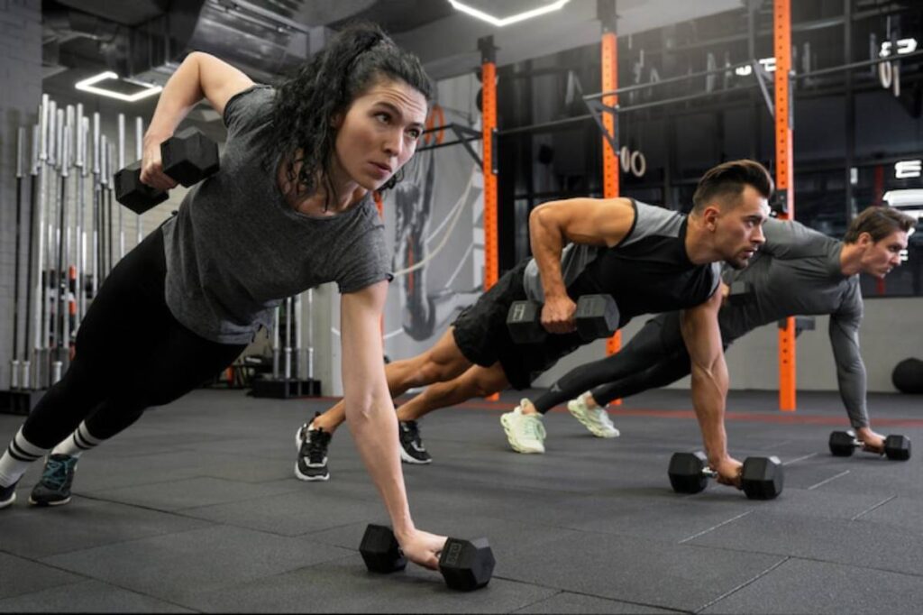 A group of people perform push-up variations using dumbbells in a stylish gym setting, showcasing strength and fitness.