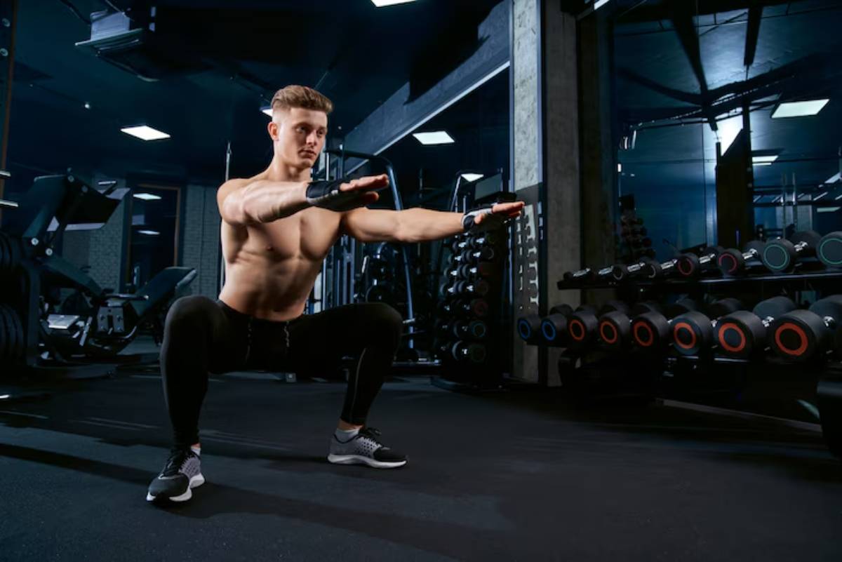 A muscular person performs a squat in a gym, surrounded by weights and fitness equipment, emphasizing strength training and exercise.