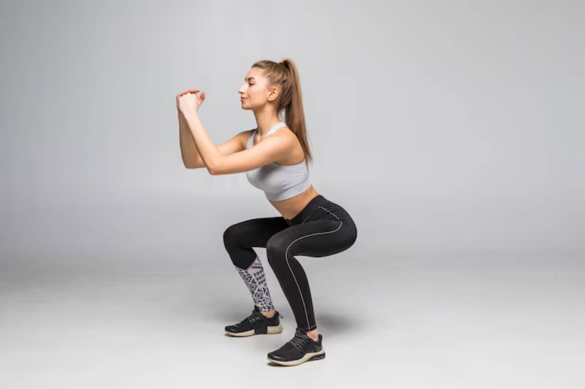 A woman in athletic wear performs a squat on a smooth, light gray background, showcasing her focused workout.