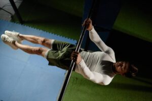 A person performs an exercise on a pull-up bar, showcasing strength and control, dressed in a fitted long-sleeve shirt and shorts.