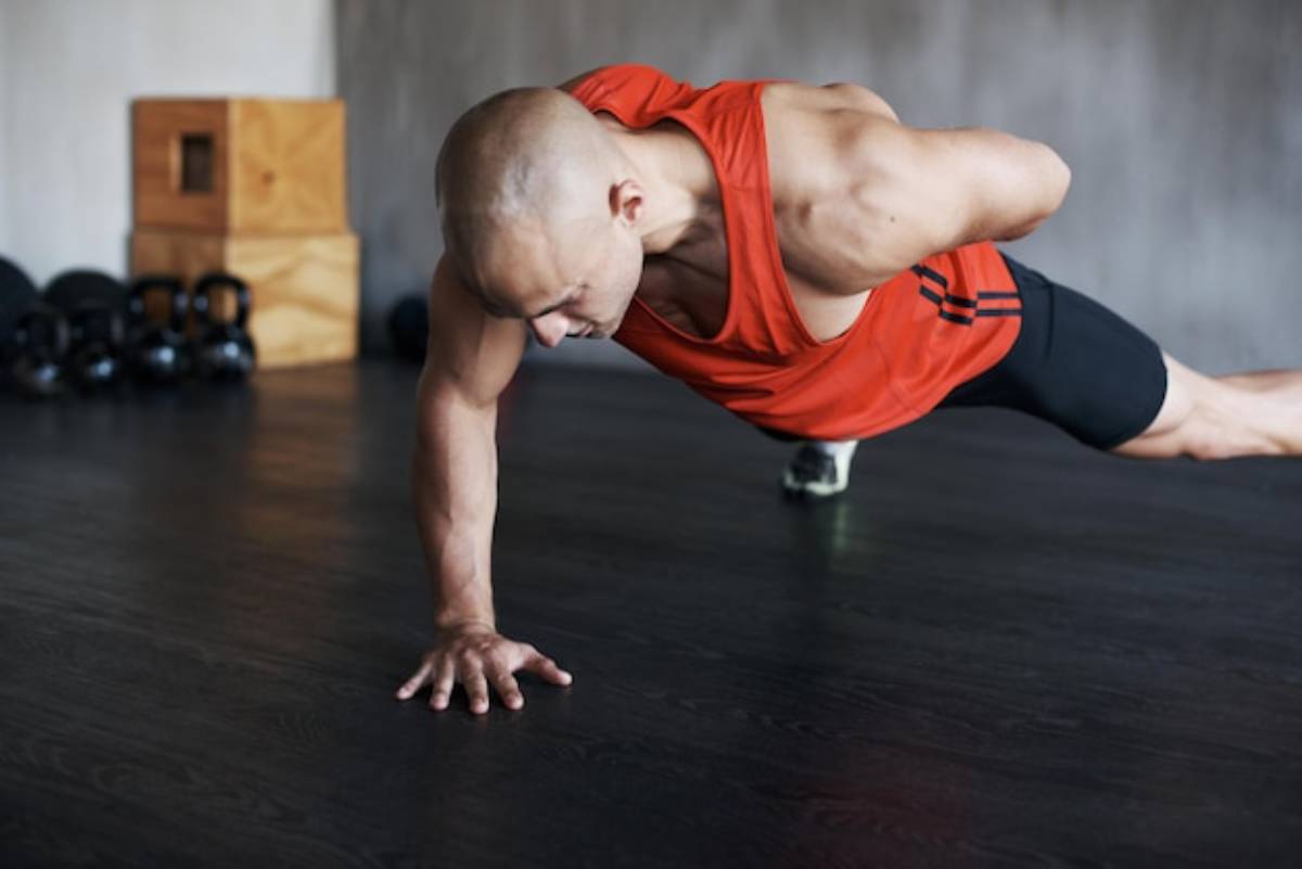 A man performs a push-up on a white background, showcasing his muscular build and athletic attire.