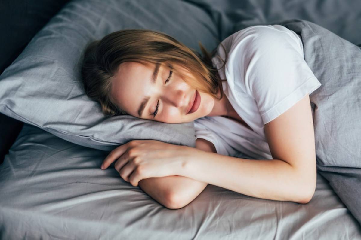 A person lies on their side in bed, resting their head on a gray pillow, surrounded by soft gray bedding.