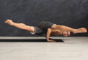 A person expertly balances on their hands in a yoga pose, with legs extended outward, showcasing strength and flexibility on a mat.