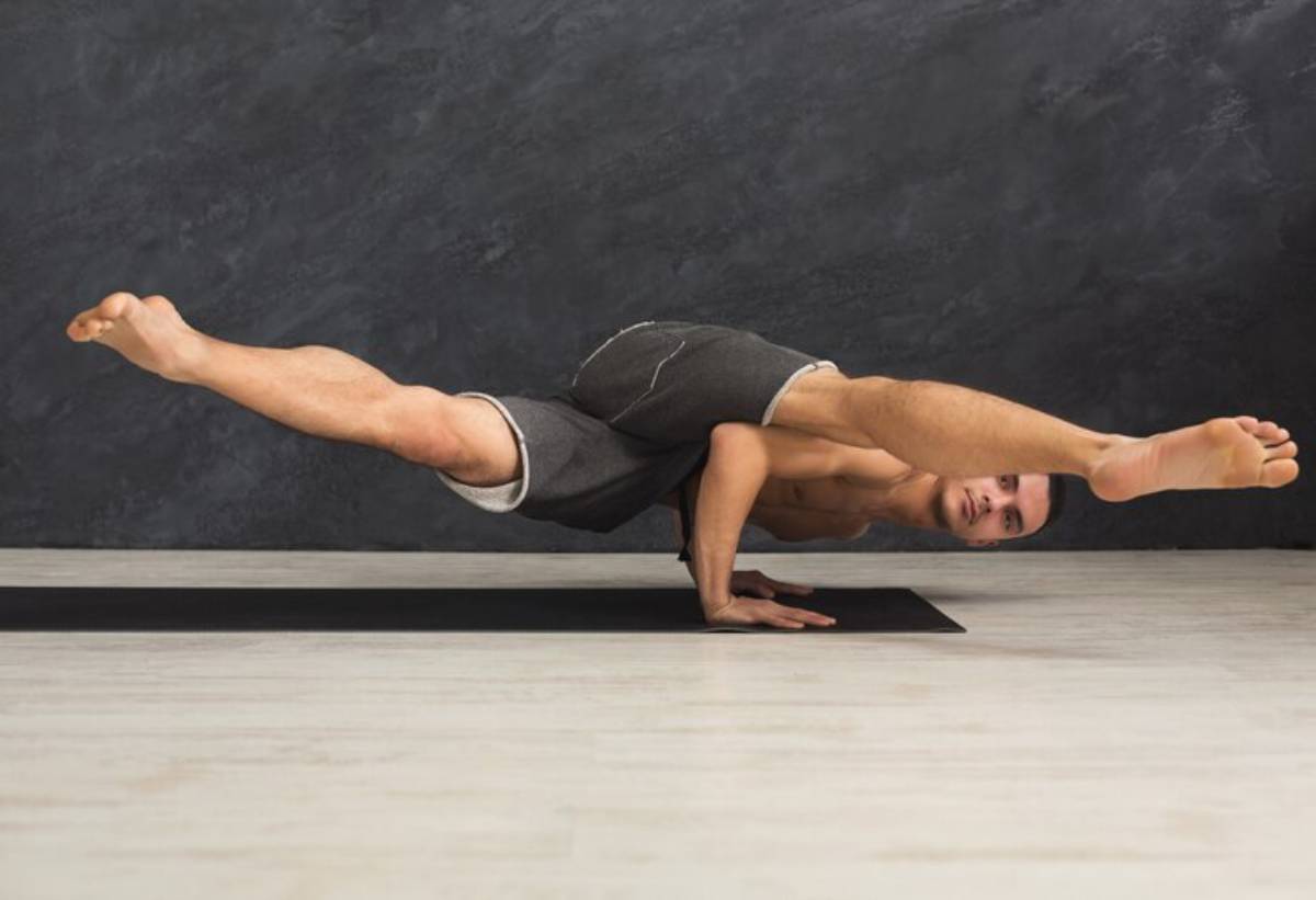 A person expertly balances on their hands in a yoga pose, with legs extended outward, showcasing strength and flexibility on a mat.